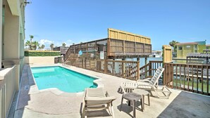 A pool area with lounge chairs and a wooden deck overlooking a body of water. - Updated Fiesta Isles Condo w/ Bay Views & Pool! (South Padre Island)