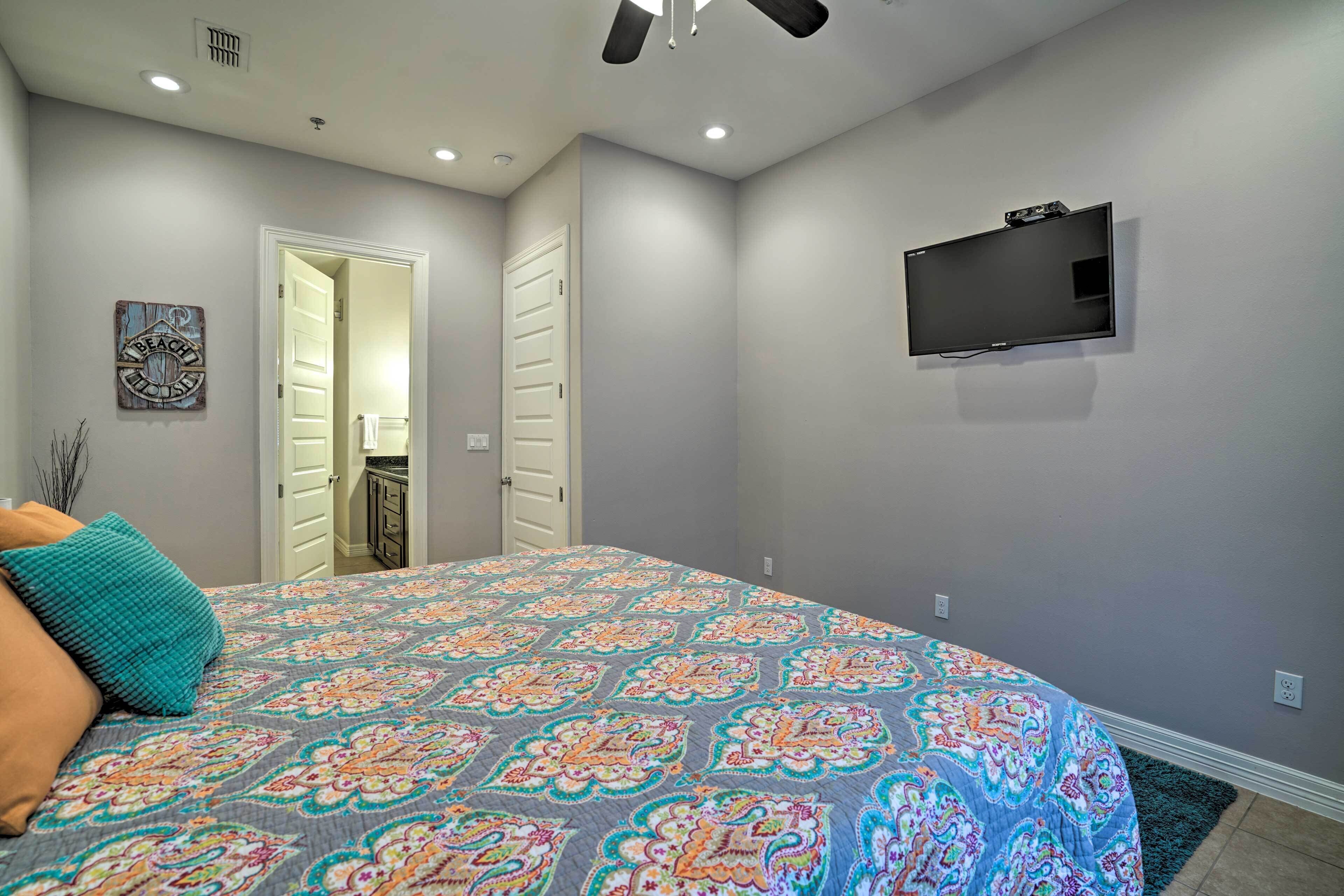 Une chambre avec une couvre-lit à motifs, un téléviseur à écran plat fixé au mur et une porte donnant sur une autre pièce.