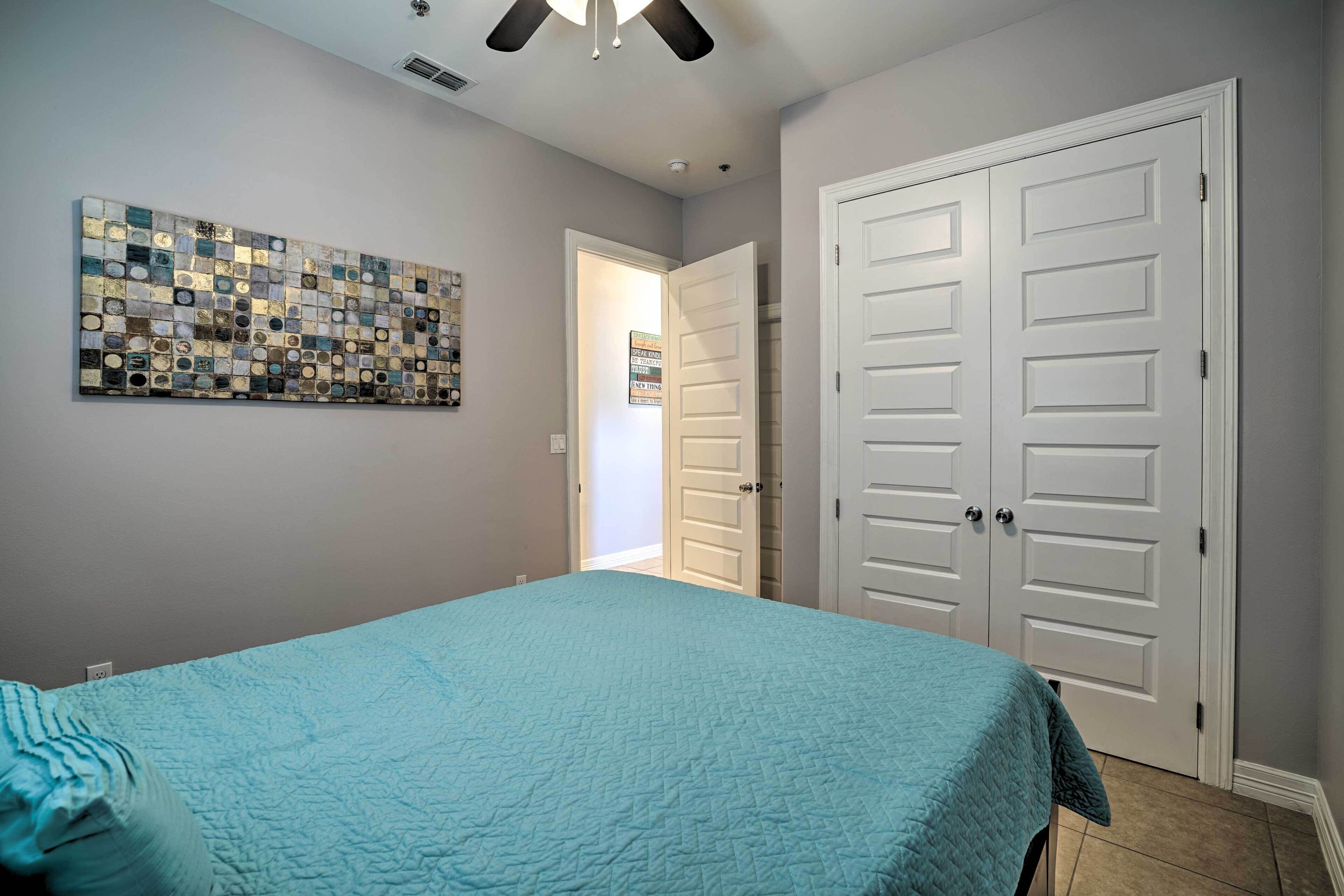 Une chambre à coucher avec un lit, un ventilateur de plafond, une œuvre d’art murale et une porte.