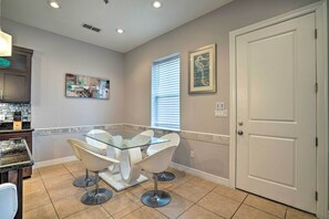 A dining area with a glass table and white chairs, a kitchen with dark cabinets, and a white door. - Updated Fiesta Isles Condo w/ Bay Views & Pool! (South Padre Island)