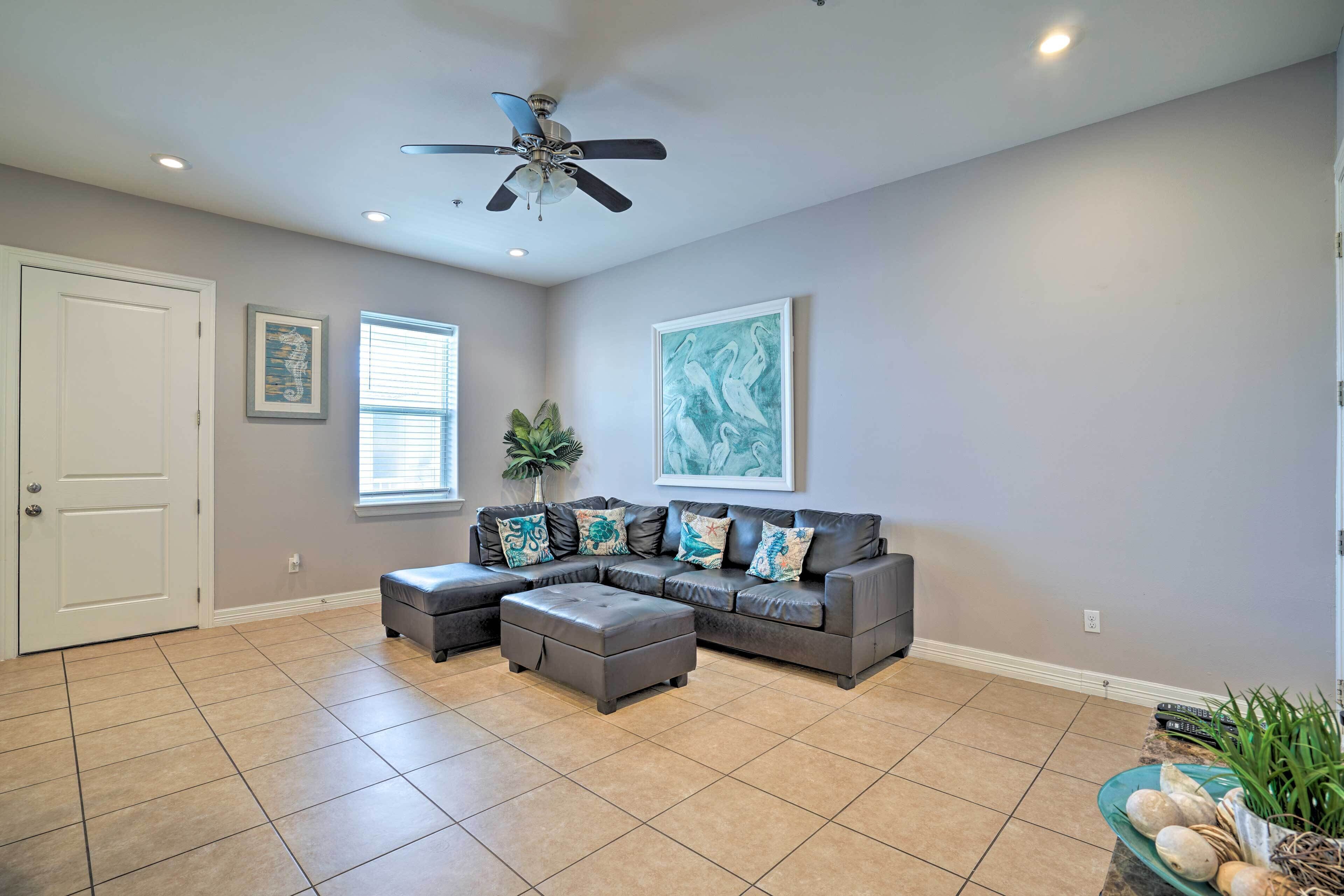 A living room with a sectional sofa, a ceiling fan, and artwork on the walls.