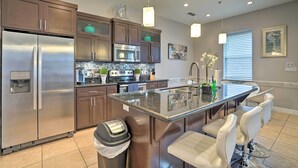 A modern kitchen with stainless steel appliances, a granite countertop island, and bar seating. - Updated Fiesta Isles Condo w/ Bay Views & Pool! (South Padre Island)