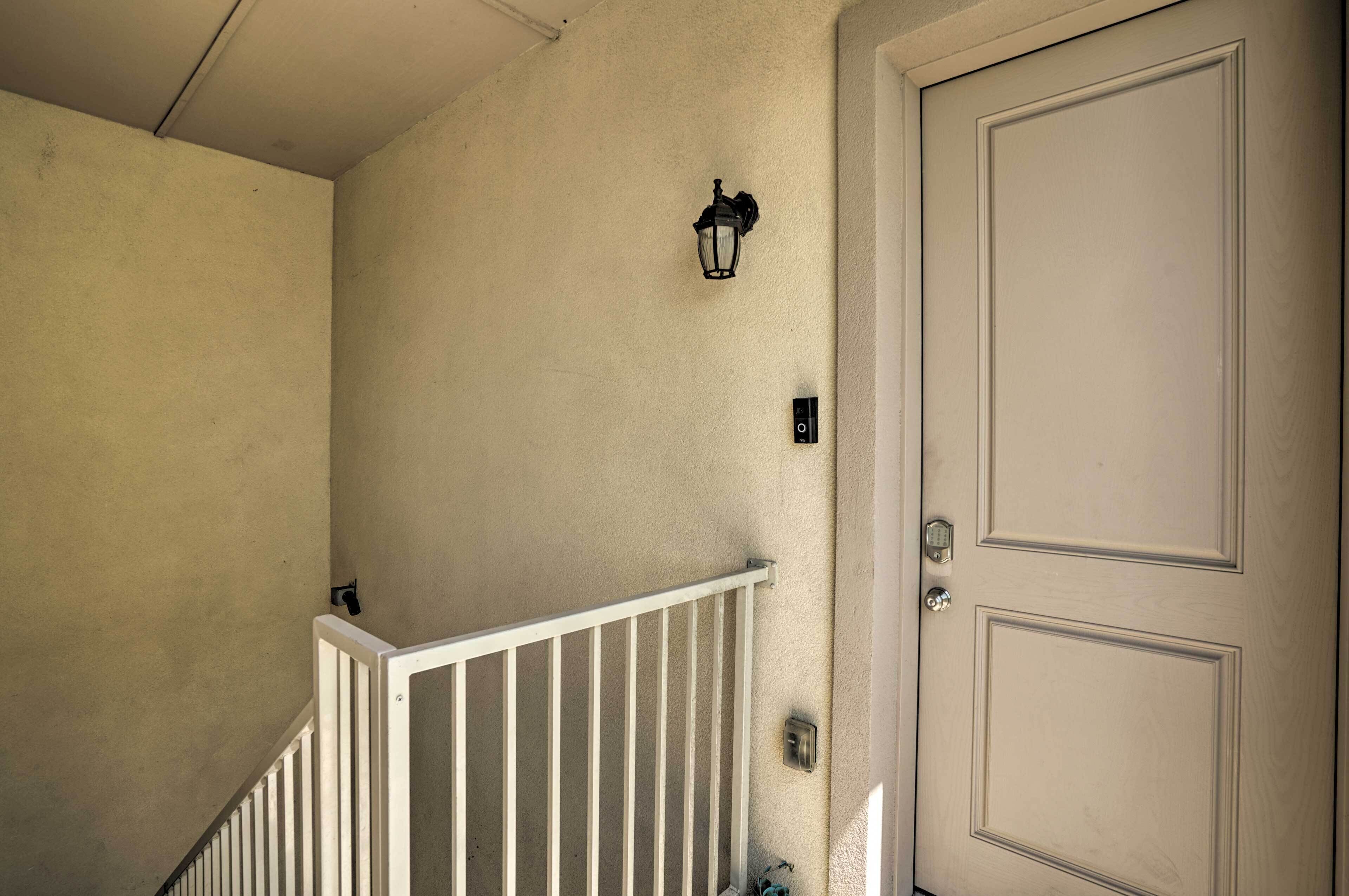 Una pared color beige con una puerta blanca, un pasamanos blanco y un aplique negro fijado a la pared.