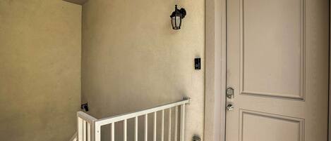 Una pared color beige con una puerta blanca, un pasamanos blanco y un aplique negro fijado a la pared.
