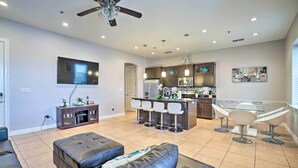 A spacious living room with a large TV, a ceiling fan, and a kitchen area with bar stools. - Updated Fiesta Isles Condo w/ Bay Views & Pool! (South Padre Island)