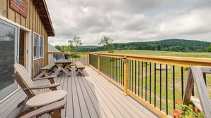 A wooden deck with Adirondack chairs and a table, overlooking a green landscape. - Lakefront Gem: Hot Tub & Game Room in Hancock (Hancock)