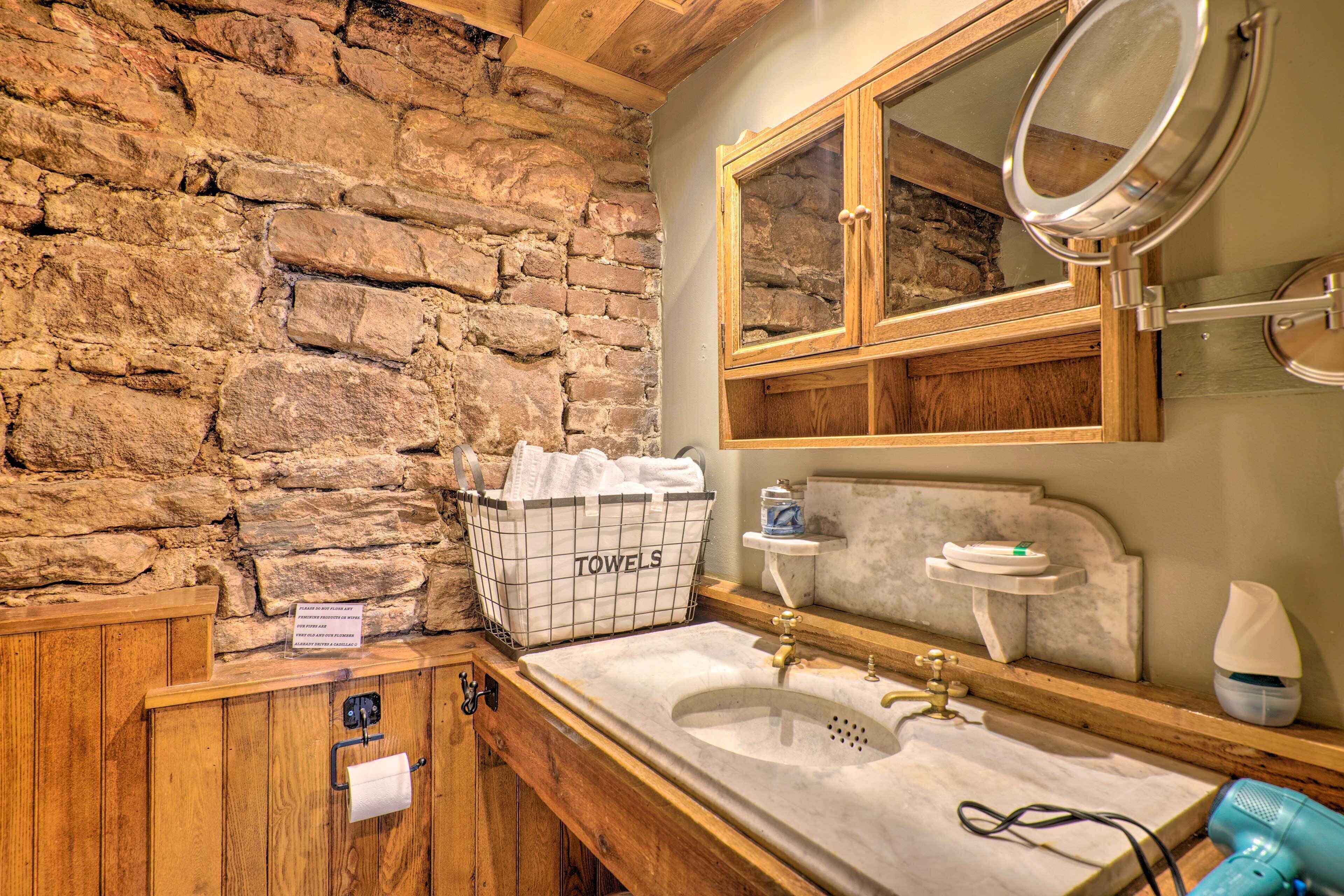 A bathroom with a stone wall, wooden cabinets, a marble sink, a towel rack, and a mirror.