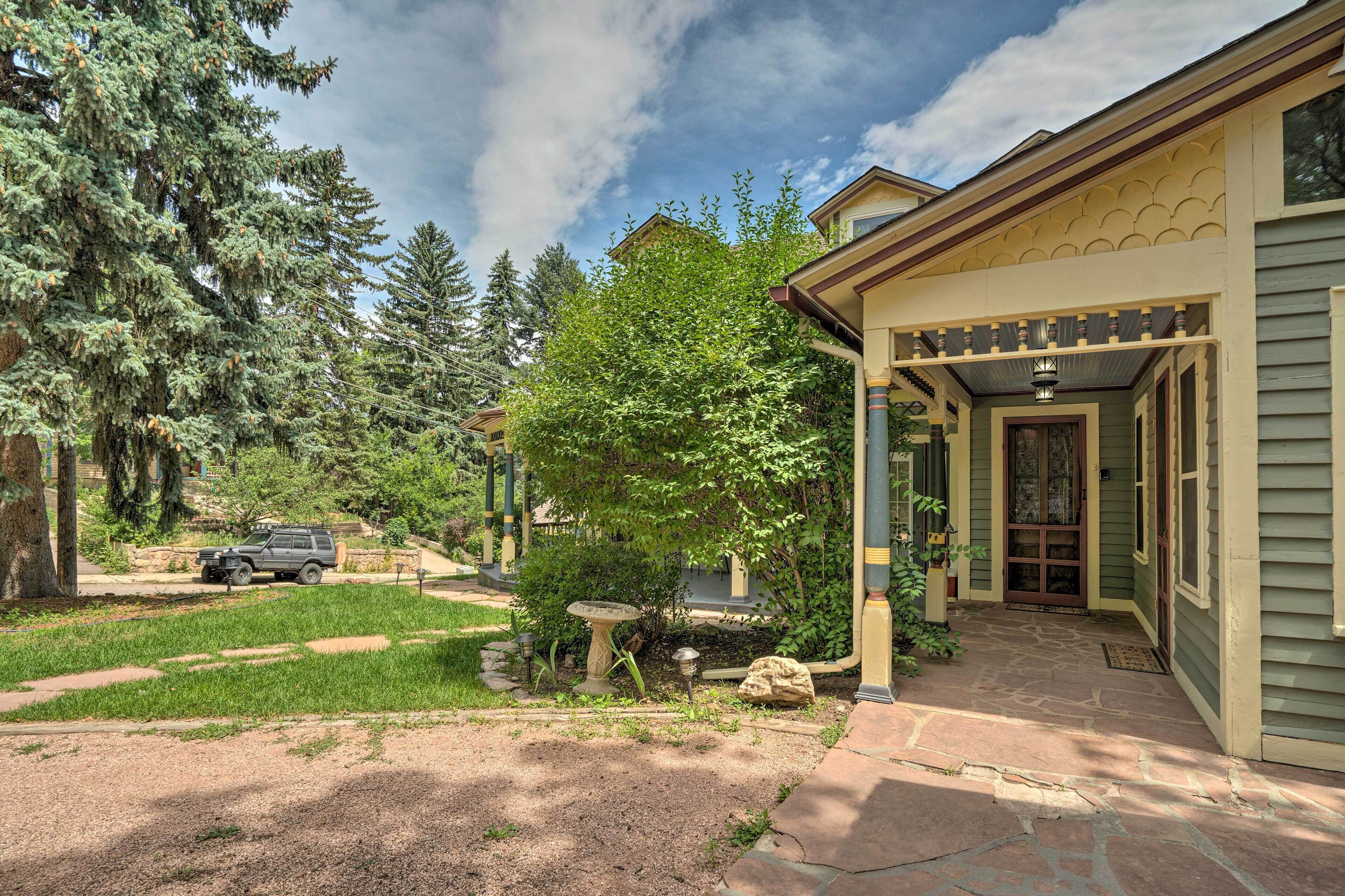 A house with a covered porch, a stone pathway, and a garden with trees and a bird bath.