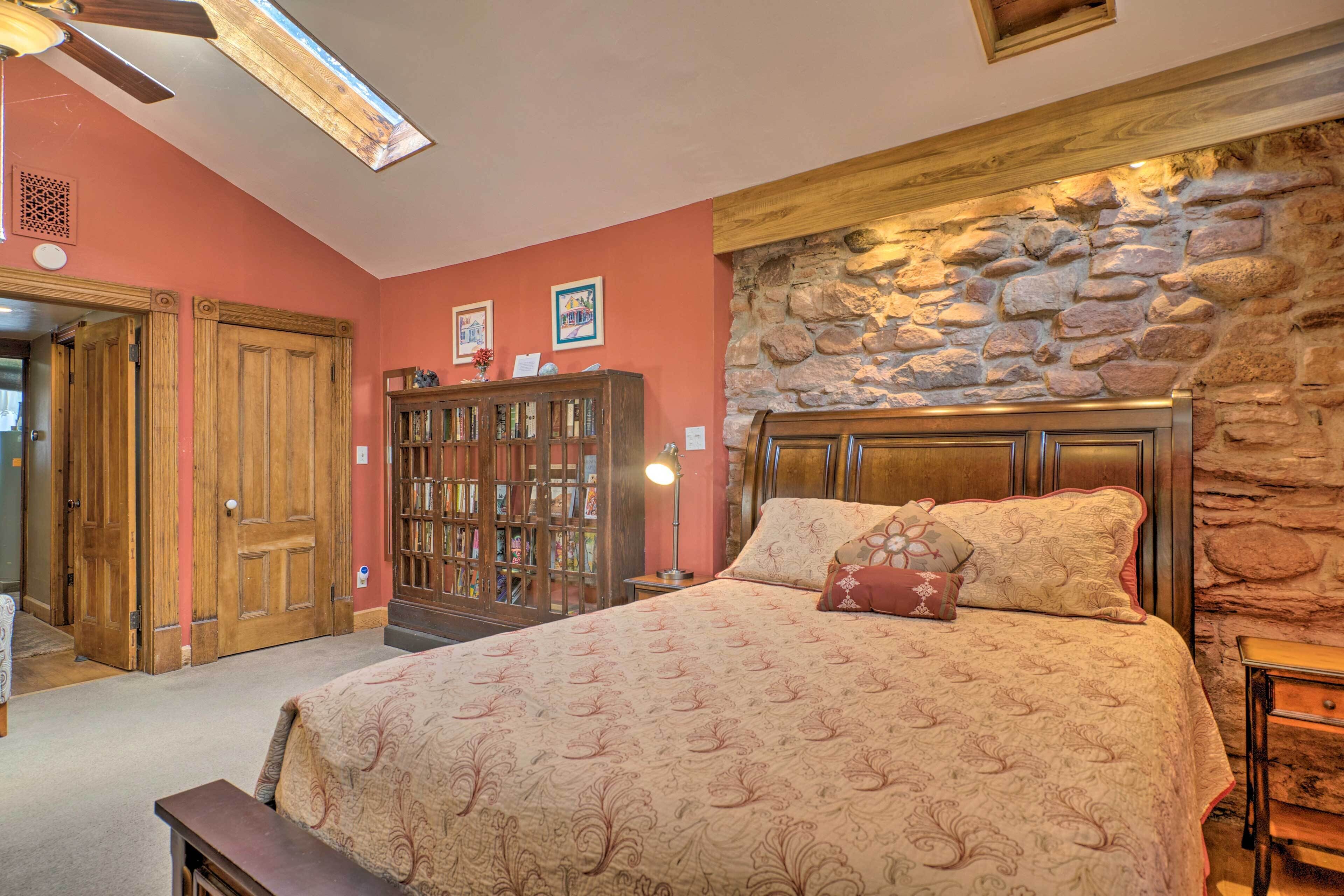 Un dormitorio con una cama grande, cabecero de madera, pared de piedra y una estantería.