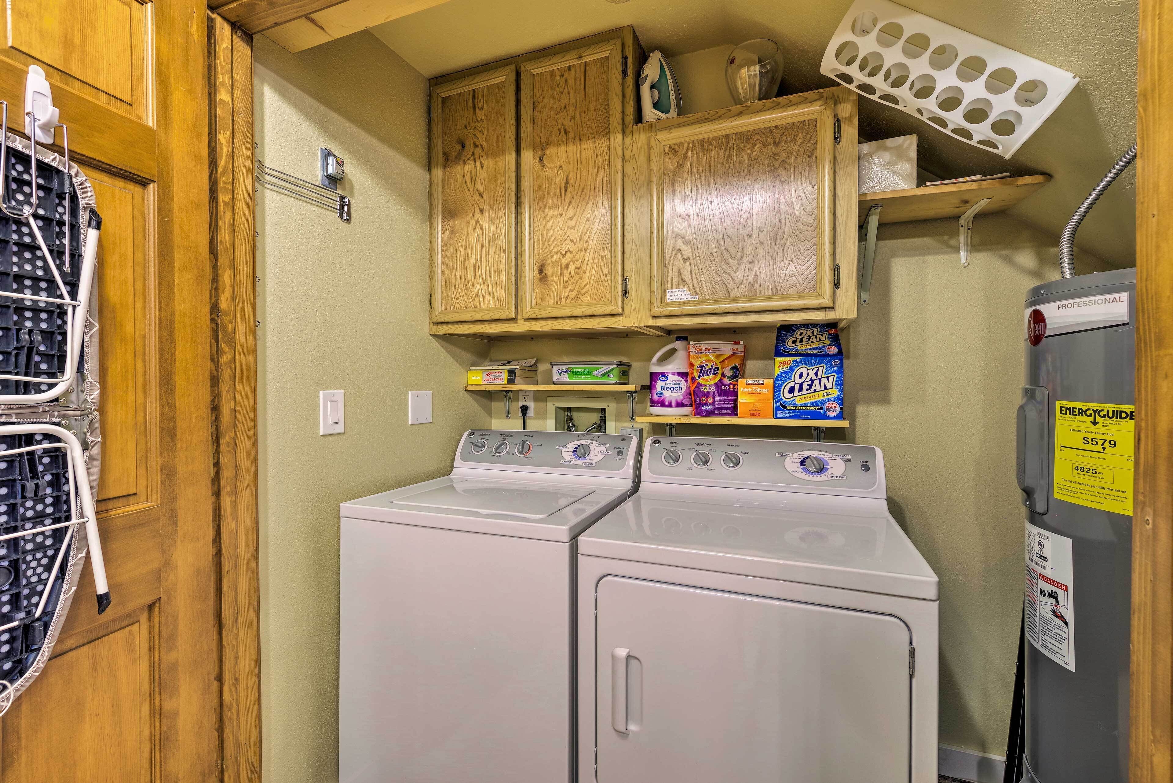 A laundry area with two front-loading washers, wooden cabinets above, and a shelf with laundry supplies.