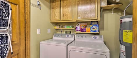 A laundry area with two front-loading washers, wooden cabinets above, and a shelf with laundry supplies.