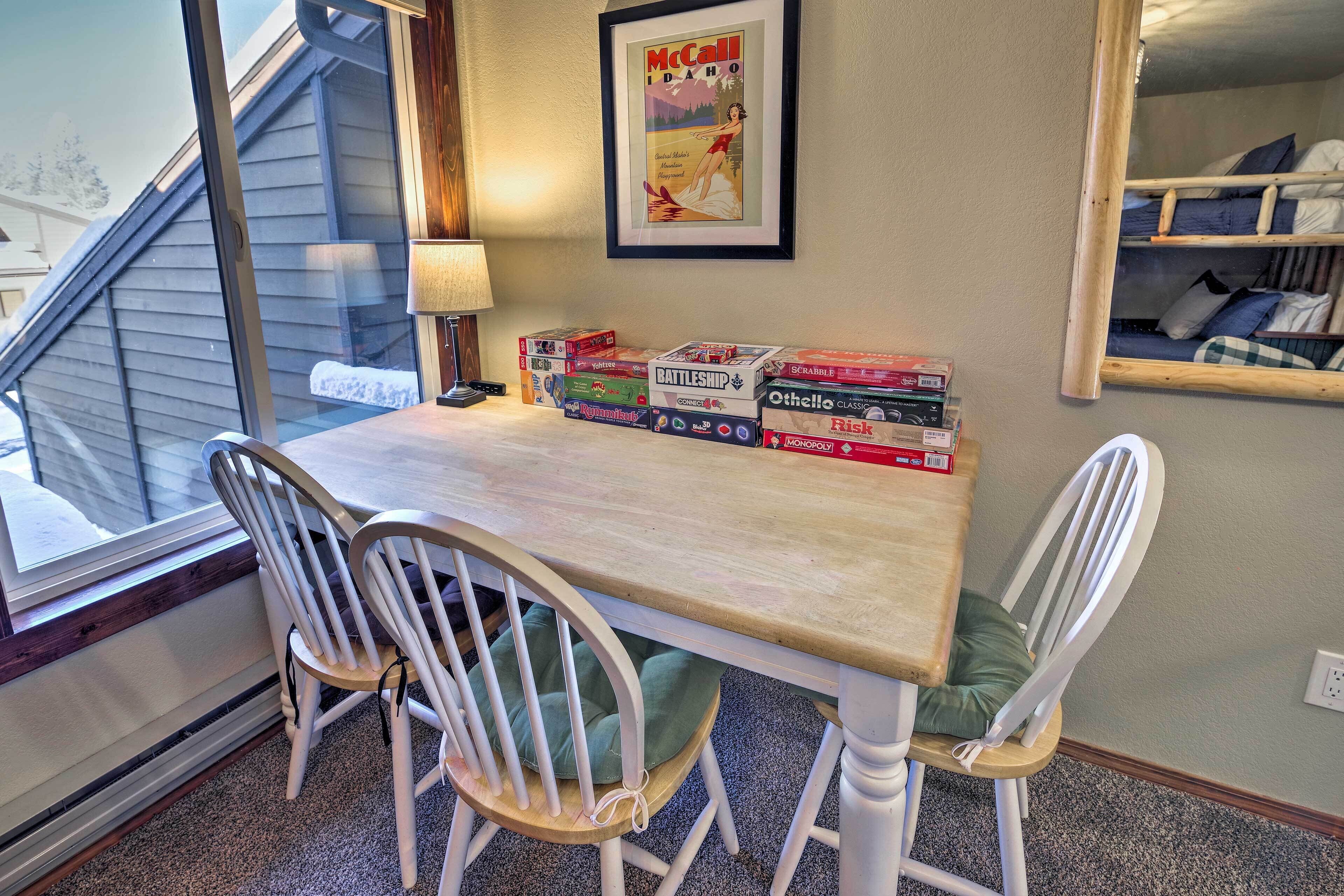 A dining area with a table, two white chairs, and a window with blinds. There are board games on the table.