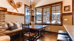 A dining area with a wooden table and chairs, a bench with cushions, and large windows with a view of the mountains. - Dog-friendly Cabin in the Heart of Grand Lake! (Grand Lake)