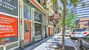 A street view with commercial buildings, including a sign for CDC Condos for sale, a sidewalk, and parked cars. - Contemporary Cincinnati Condo - Pets Allowed! (Cincinnati)