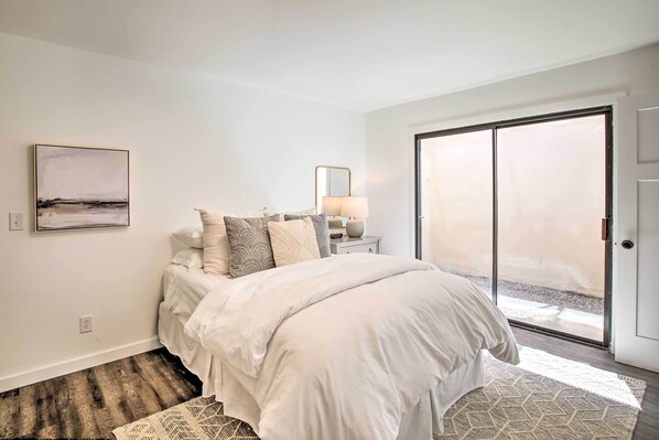 A bedroom with a bed, a nightstand, a lamp, a large window, and a view of the outdoors.