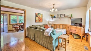 Una sala de estar acogedora con un sofá, una mesa de comedor con sillas, un aparador de madera y un televisor.