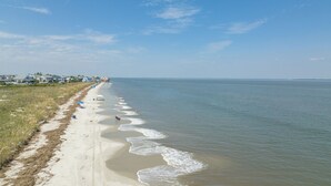 A beach with a long stretch of sand, a few umbrellas, and houses in the background. - Oceanfront St Helena Island Condo w/ Beach Access! (Harbor Island)
