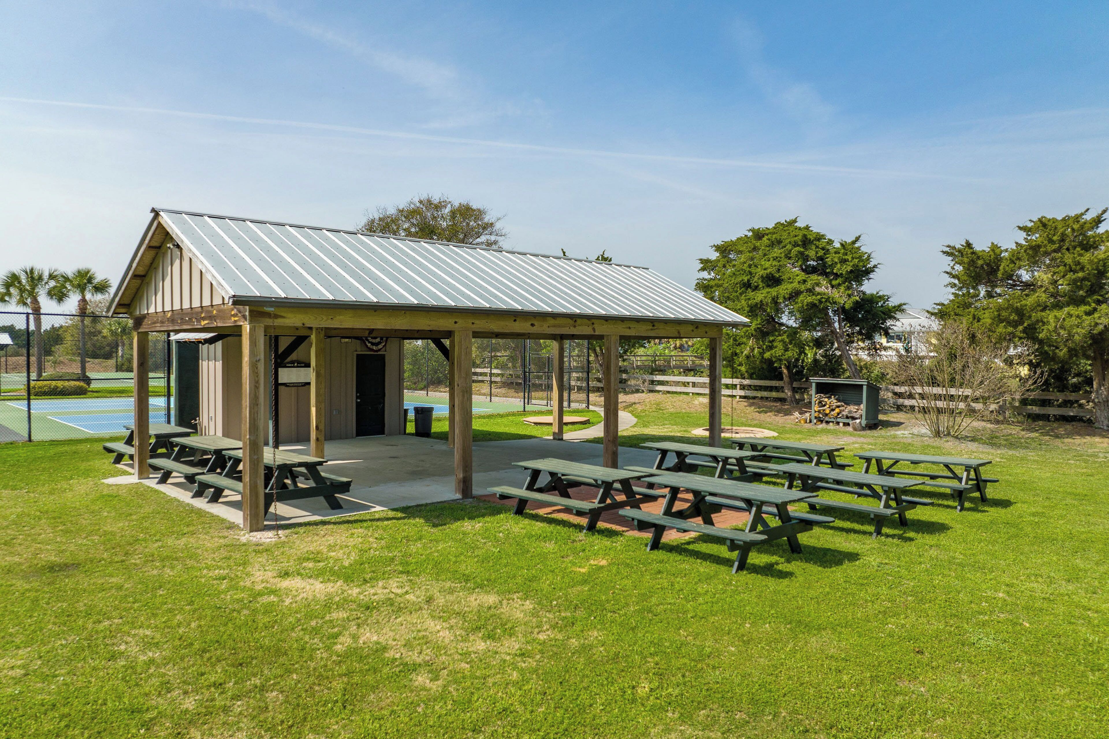 A covered picnic area with benches and a small building, surrounded by grass and trees.