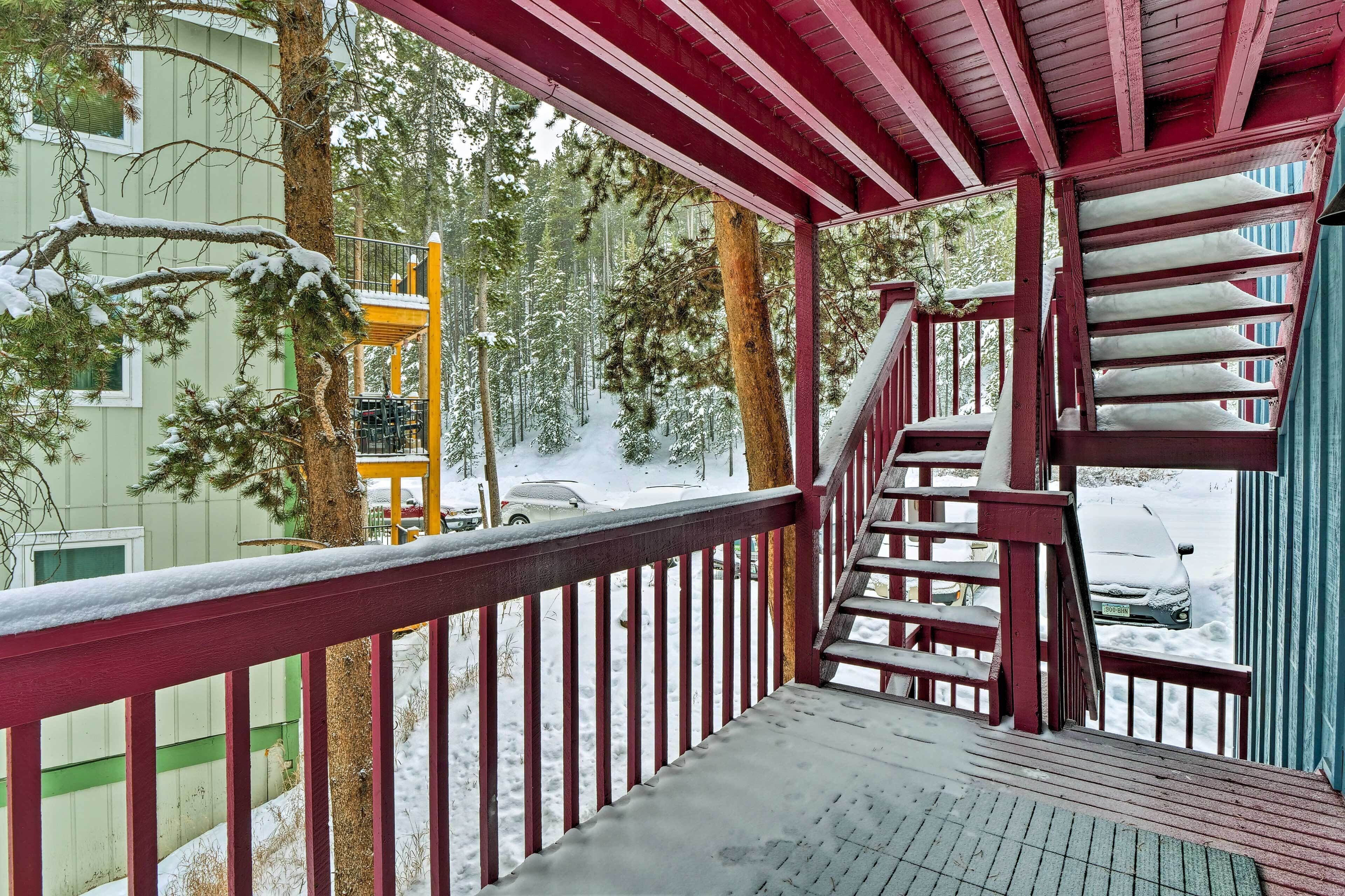 A wooden deck with a red railing overlooking a snowy landscape and a building.