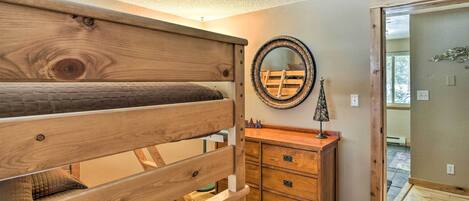 A bedroom with a wooden bed, a dresser, a mirror, and a door leading to another room.