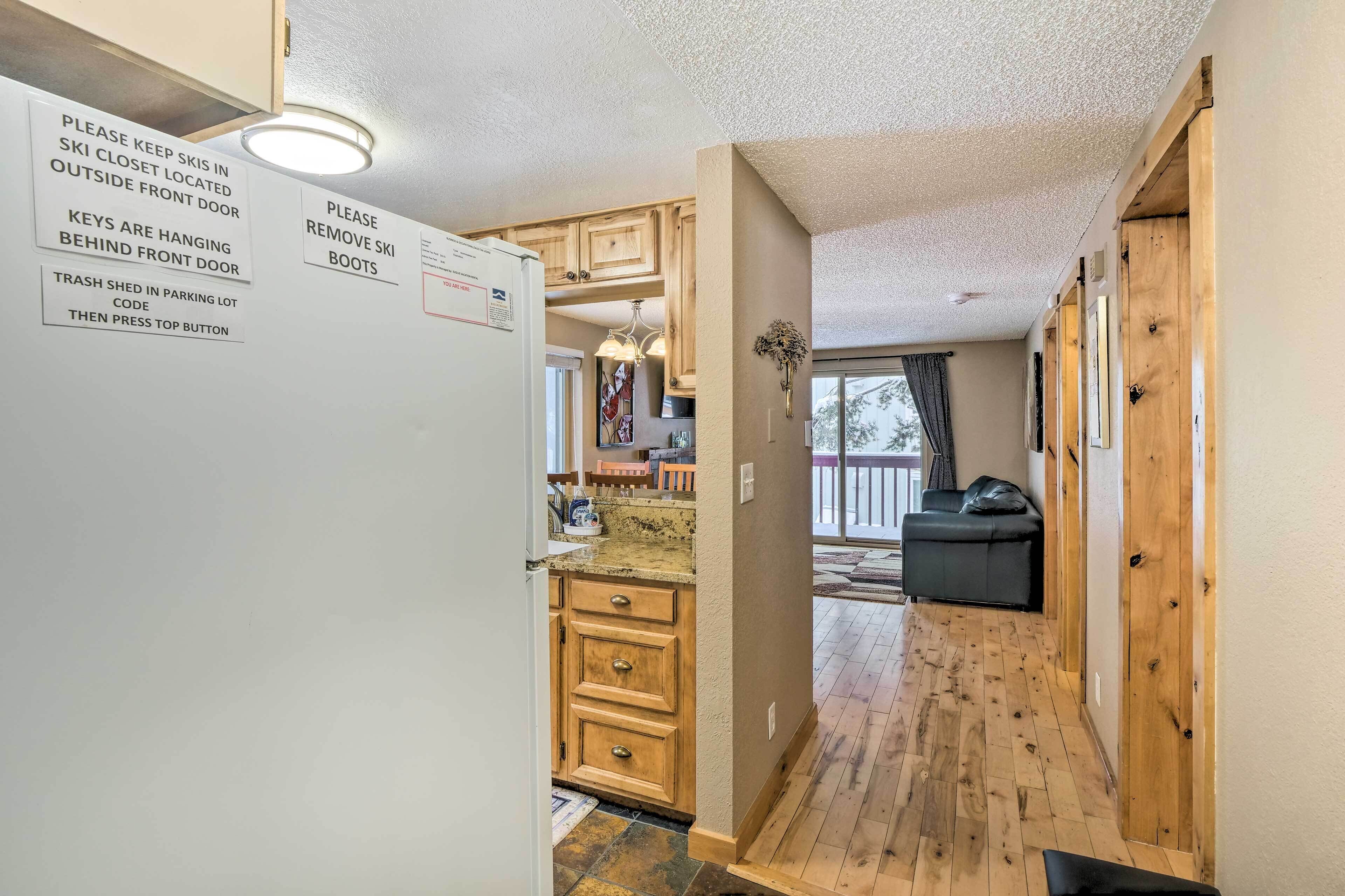 A compact kitchen with wooden cabinets, a refrigerator, and a sign with ski-related instructions.