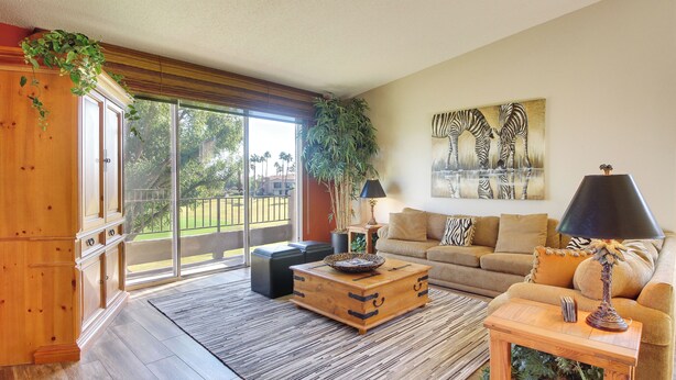 A spacious living room with a large sliding glass door leading to a balcony, a wooden coffee table, a sofa, and a lamp. - 112117: Spacious 3 BR La Quinta Condo on PGA West! (La Quinta)