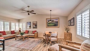 A spacious living room with a wooden floor, a ceiling fan, a dining area with striped chairs, and large windows with blinds. - 112117: Spacious 3 BR La Quinta Condo on PGA West! (La Quinta)