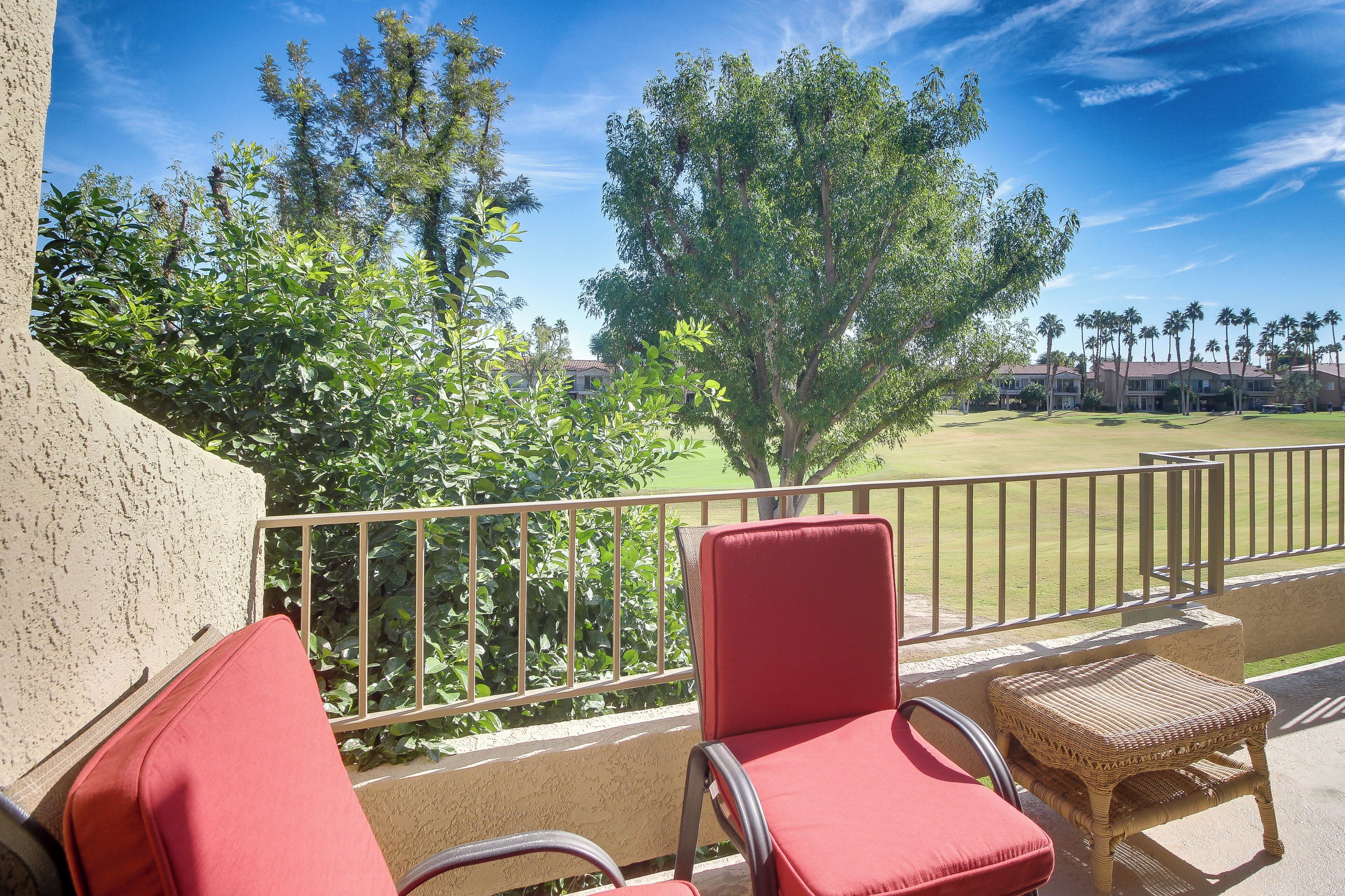Ein Balkon mit roten Stühlen und einem Korbstuhl, mit Blick auf einen Golfplatz und Palmen.