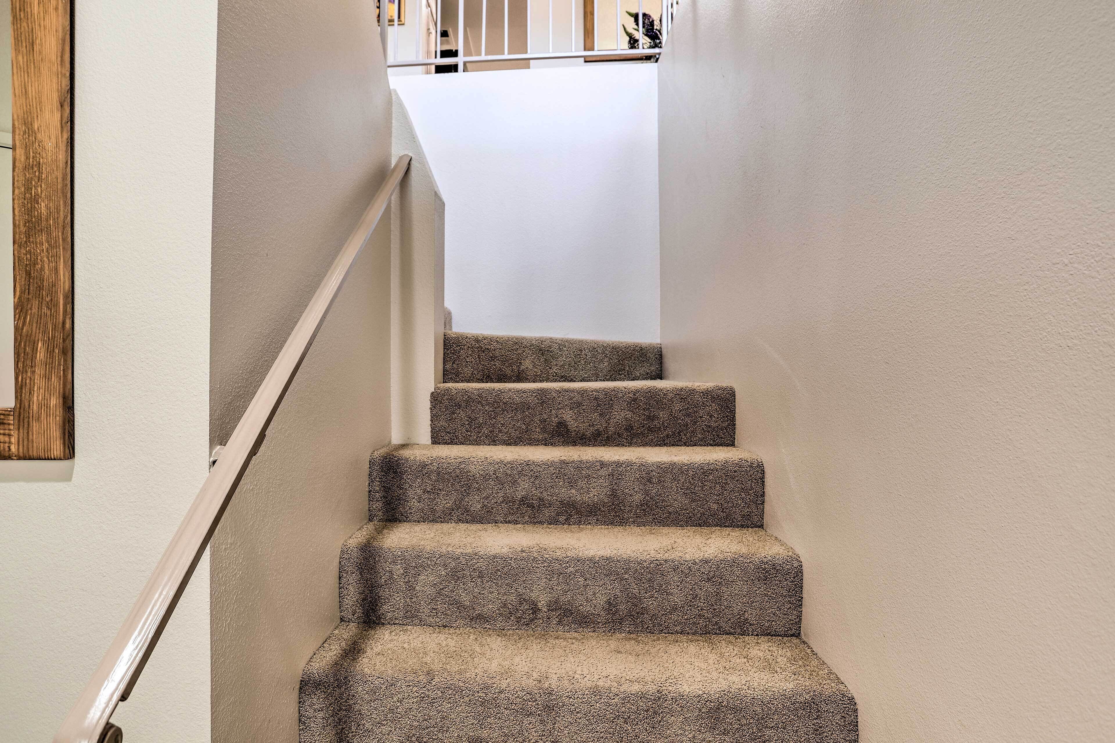 Un escalier recouvert de moquette, avec une rampe et un mur blancs.