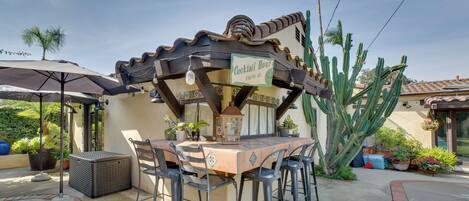 An outdoor patio area with a table and chairs, a sign indicating 'Cocktail Hour', and a large cactus in the background.