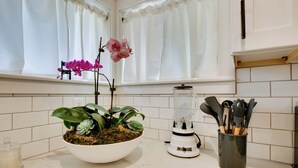 Een keuken met een wit aanrecht, een blender, een houder voor keukengerei en een potplant met orchideeën.