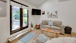 Een moderne woonkamer met een bank, een salontafel, een aan de muur bevestigde televisie, en een raam met uitzicht op groen.