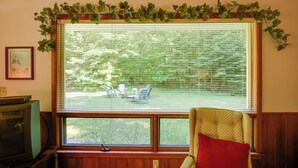 A room with a large window covered by blinds, a television, and a chair with a red cushion. - 'cherry Cottage' - Walk to Peninsula State Park! (Ephraim)