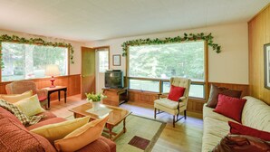 A cozy living room with a television, comfortable seating, and large windows with greenery. - 'cherry Cottage' - Walk to Peninsula State Park! (Ephraim)