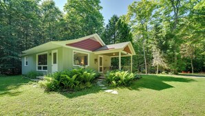 A small, single-story house with a covered porch, surrounded by lush greenery and trees. - 'cherry Cottage' - Walk to Peninsula State Park! (Ephraim)