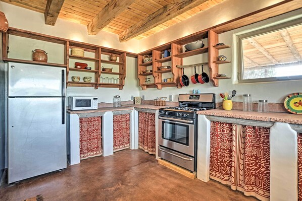 Une cuisine avec des meubles en bois, un réfrigérateur en acier inoxydable, un four à micro-ondes, une cuisinière et des rideaux à motifs.