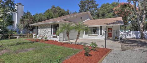 A single-story house with a stone facade, a front porch, and a well-maintained lawn with red mulch and gravel pathways.
