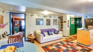 A cozy living room with a sofa, a dining table with a basket of fruit, a kitchen area with a green door, and a patterned rug. - Dunsmuir Apartment ~ 17 Mi to Mt Shasta Ski Park! (Dunsmuir)