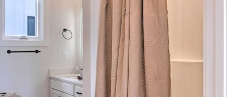 A bathroom with a white sink, a mirror, a towel rack, and a beige shower curtain.