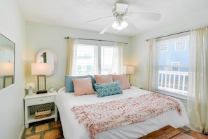 A bedroom with a bed, two bedside tables, a nightstand, a ceiling fan, and a window with curtains.