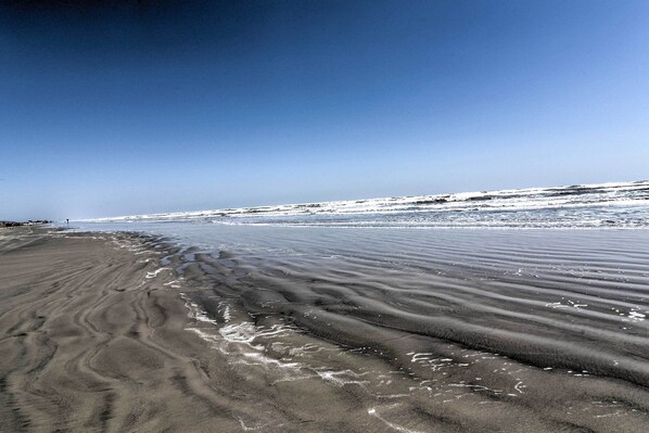 A beach with wet sand patterns and a clear sky.