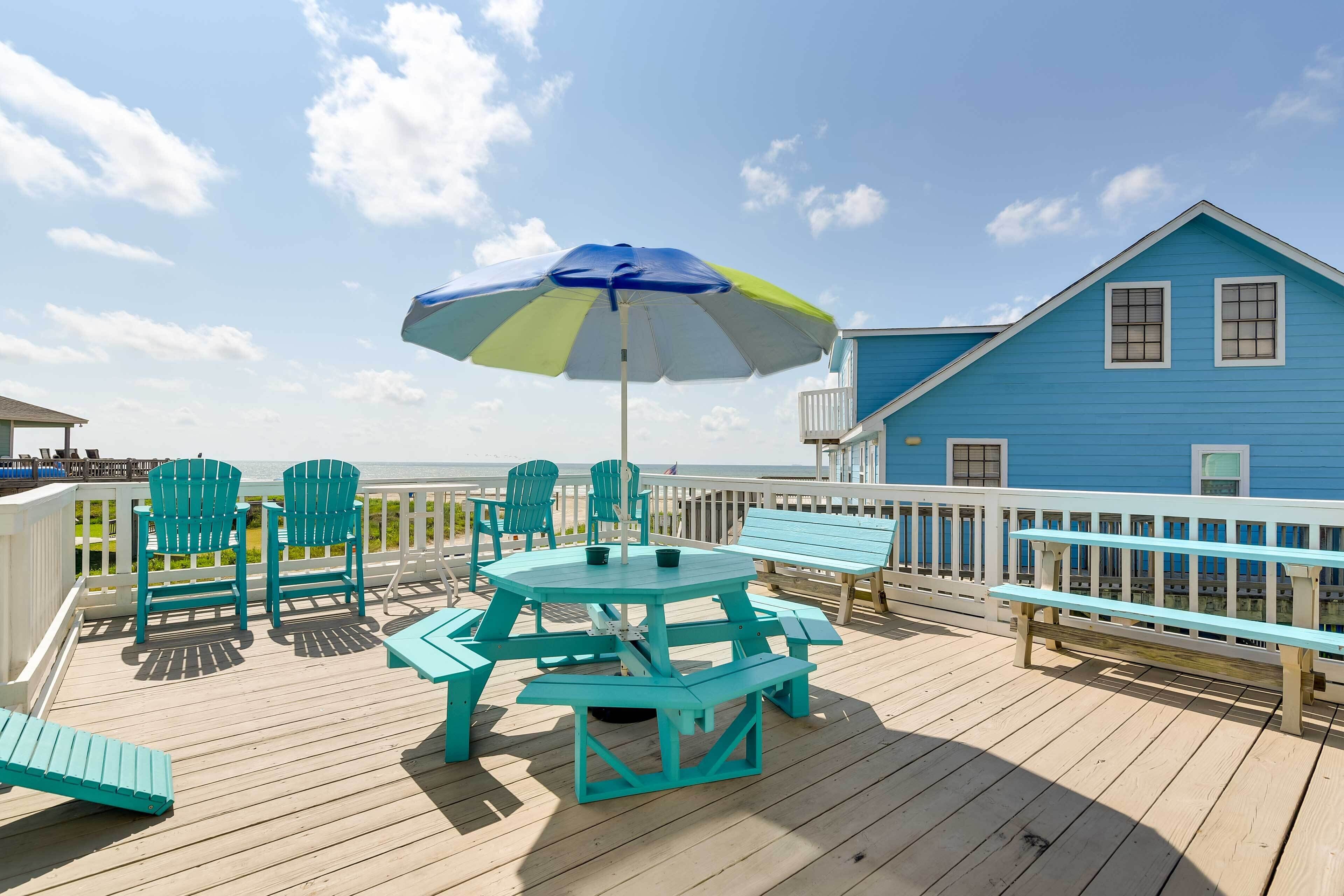 Une terrasse avec des chaises turquoise, une table de pique-nique et un parasol bleu.