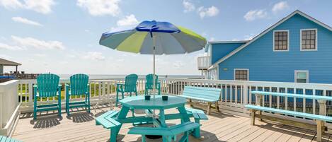 Une terrasse avec des chaises turquoise, une table de pique-nique et un parasol bleu.