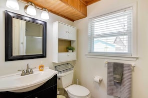 A bathroom with a white sink, a mirror, a toilet, and a window with blinds.