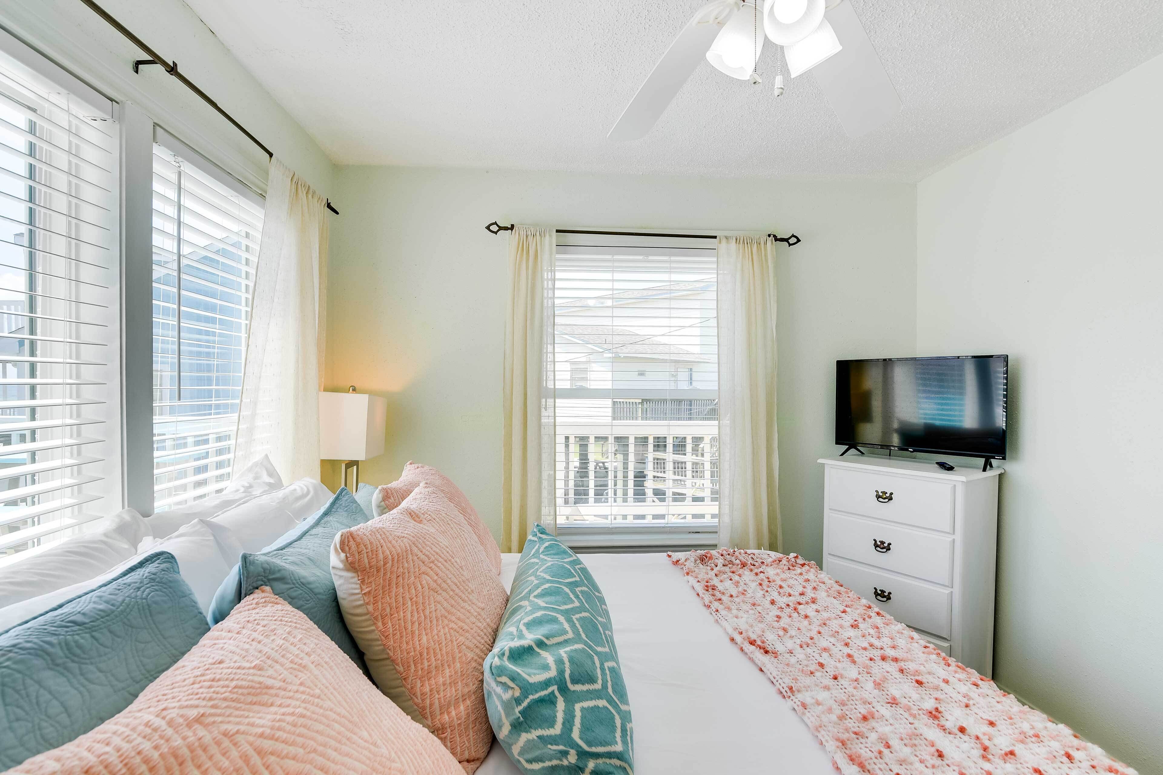 Une chambre à coucher avec un lit, des oreillers, une télévision, une commode et une fenêtre avec des rideaux.