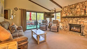 A cozy living room with a stone fireplace, comfortable seating, and a large window offering a view of the outdoors.