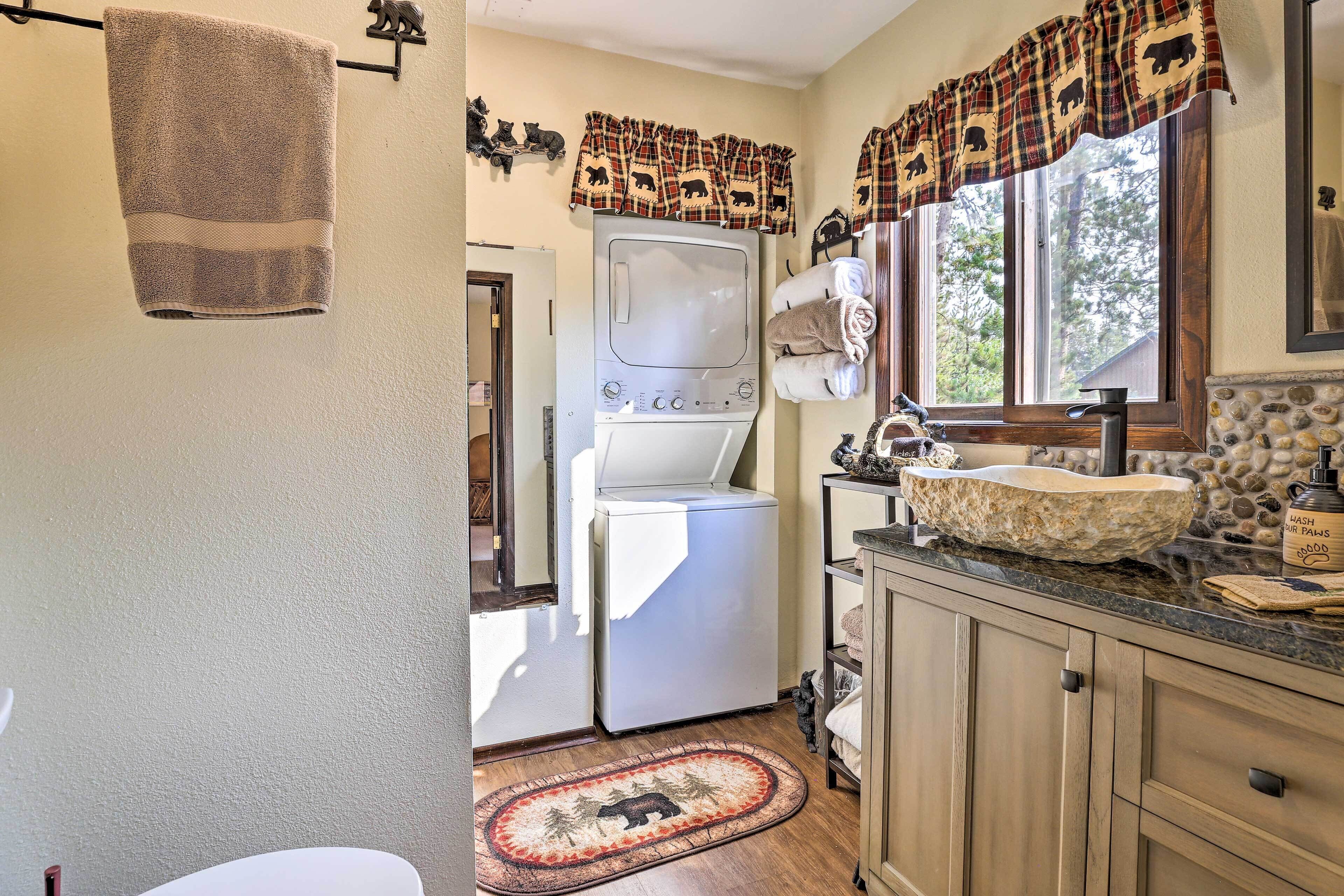 A laundry area with a washing machine, a sink with a stone basin, and a window with a plaid curtain.