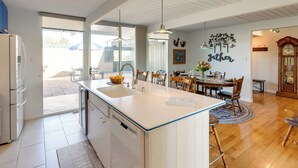 A modern kitchen with a central island, white cabinetry, and a dining area with wooden chairs and a table. - Home w/ Views & Fire Pit, 10 Mi to Aztec Ruins! (Farmington)