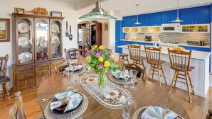 A dining area with a wooden table set for six, surrounded by chairs, a large vase with flowers, and a cabinet with glass doors. - Home w/ Views & Fire Pit, 10 Mi to Aztec Ruins! (Farmington)
