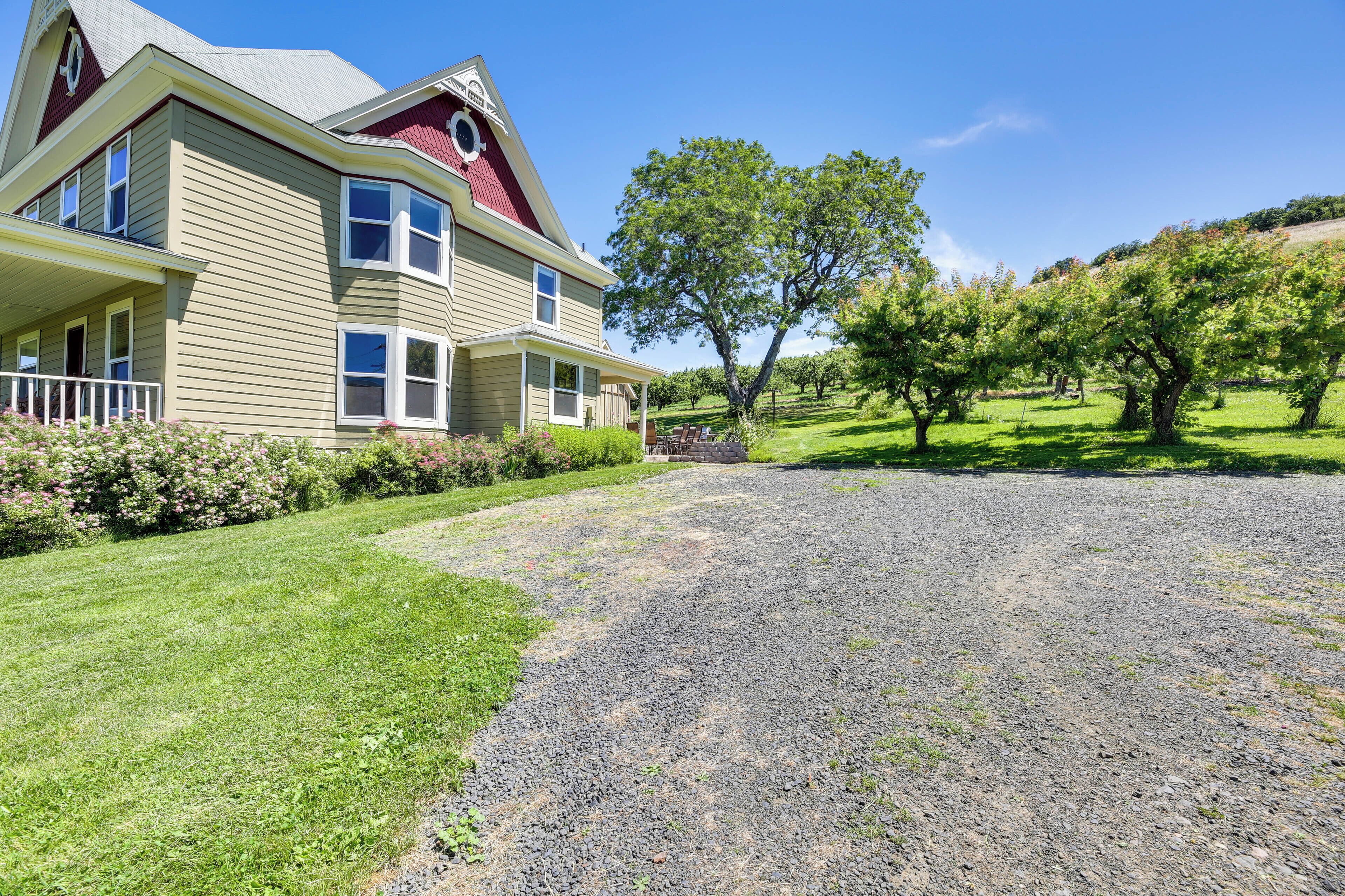 A two-story house with a red roof, a front porch, and a gravel driveway.